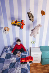Little boy meditating on his bed with toys flying over his head - LJF01486