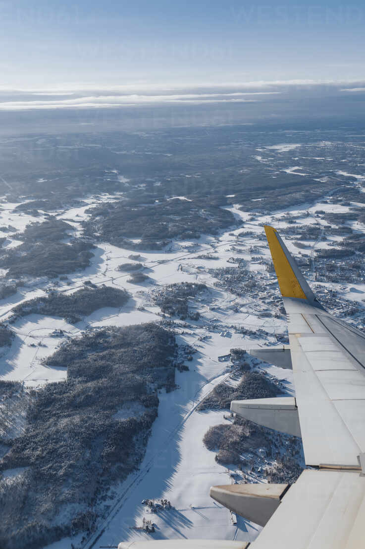 Finland, Wing of airplane flying over forested landscape in winter stock  photo
