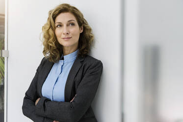 Successful businesswoman leaning on wall, with arms crossed - BMOF00312