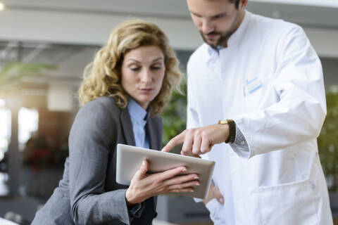 Geschäftsfrau mit Tablet und Arzt im Gespräch im Krankenhaus, lizenzfreies Stockfoto