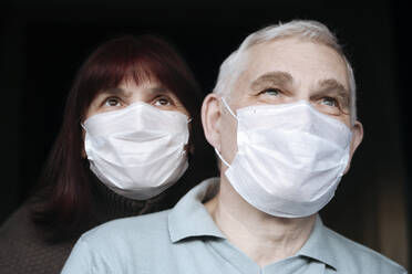 Portrait of senior couple wearing masks at home - EYAF00993