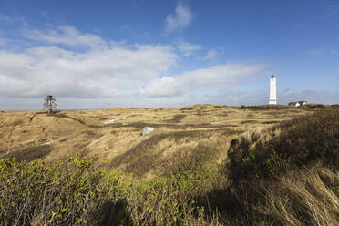 Dänemark, Romo, Blavand, Wolken über grasbewachsener Küstenlandschaft mit Leuchtturm im Hintergrund - ASCF01183