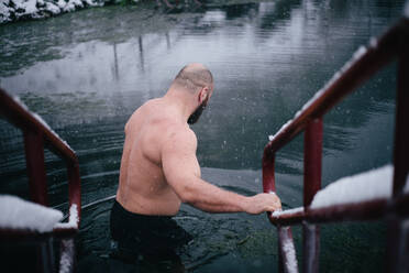 Rear View Of Shirtless Man Moving In Lake During Snowfall In Winter - EYF01981