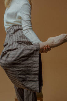 Midsection of Woman Standing On One Leg Against Brown Background - EYF02000