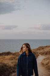 Junge Frau zu Fuß auf Schotterstraße gegen Meer und Himmel - EYF02038