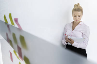 Young businesswoman, standing in office, taking notes from adhesive notes - BMOF00333