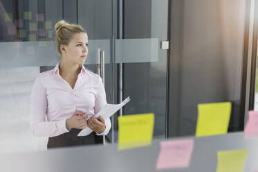 Young businesswoman, standing in office, carrying documents - BMOF00335