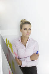 Young businesswoman, standing in office, leaning on wall, thinking - BMOF00338