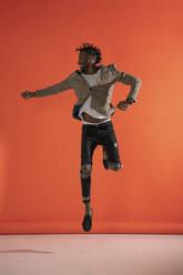 Junger Mann springt und tanzt vor einer orangefarbenen Wand - VPIF02193