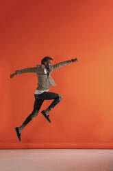Junger Mann springt und tanzt vor einer orangefarbenen Wand - VPIF02194