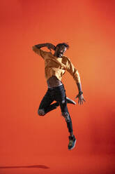 Young man jumping and dancing in front of orange wall - VPIF02197