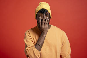 Young man covering his face in front of orange wall - VPIF02202