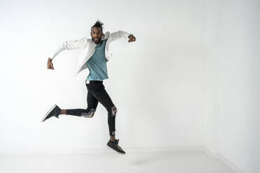 Junger Mann springt und tanzt vor einer weißen Wand - VPIF02207