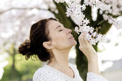 Reife Frau mit geschlossenen Augen riecht an Baumblüten, lizenzfreies Stockfoto