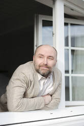 Portrait of relaxed mature man leaning out of window - VYF00085