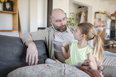 Vater und kleine Tochter sitzen zusammen auf der Couch zu Hause und haben Spaß - VYF00086