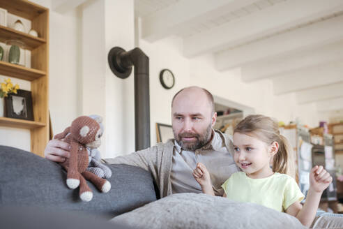 Vater und kleine Tochter sitzen zusammen auf der Couch zu Hause und spielen mit Spielzeug - VYF00087