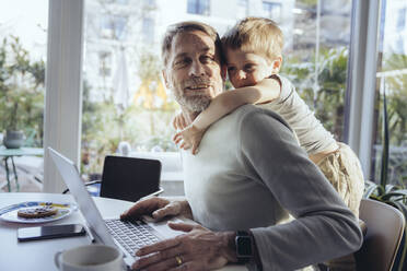 Little boy hugging father from behind, while working from home - MFF05166