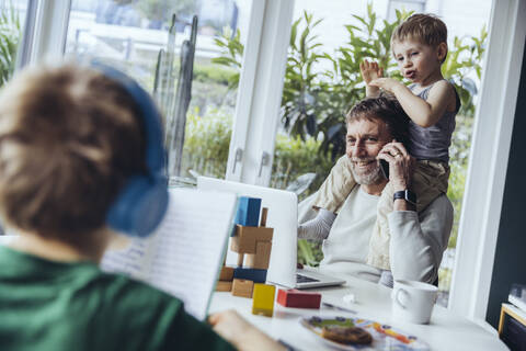 Vater arbeitet von zu Hause aus, telefoniert, während die Kinder spielen, lizenzfreies Stockfoto