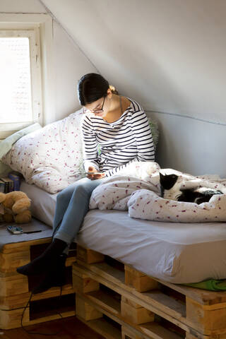 Mädchen sitzt zu Hause auf dem Bett und schaut auf ihr Handy, lizenzfreies Stockfoto