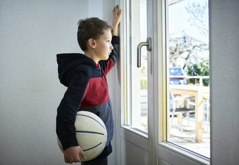 Trauriger Junge mit Basketball schaut aus dem Fenster, lizenzfreies Stockfoto