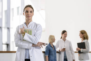 Porträt einer Ärztin im Krankenhaus mit Kollegen im Hintergrund - BMOF00356