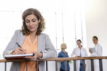 Geschäftsfrau macht sich Notizen mit Ärztinnen im Hintergrund - BMOF00358