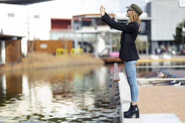 Smiling young woman taking selfie with smartphone near water - JSRF00948