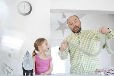 Grimacing father and daughter ironing together at home - VYF00102