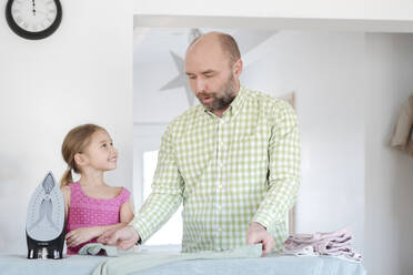 Vater und lächelnde Tochter bügeln gemeinsam zu Hause - VYF00103