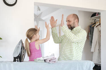 Father and daughter high fiving after ironing at home - VYF00107