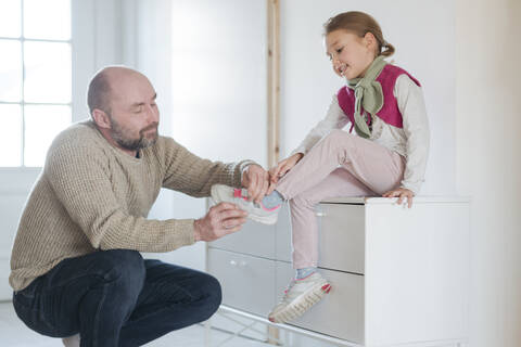 Vater hilft Tochter beim Anziehen der Schuhe zu Hause, lizenzfreies Stockfoto