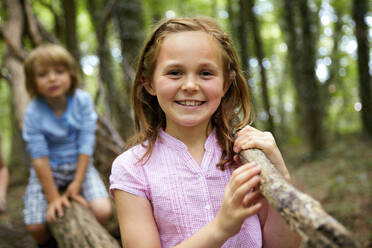 Portrait of smiling girl carrying log in forest - AUF00192