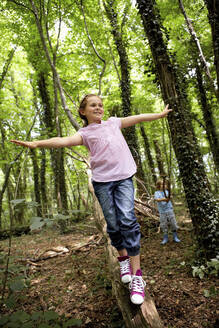 Mädchen balanciert auf Baumstamm im Wald - AUF00195