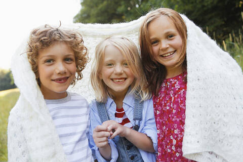 Portrait of happy children wrapped in blanket outdoors stock photo