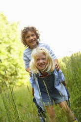 Girl carrying boy piggyback on a meadow - AUF00205