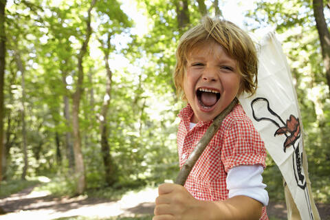 Porträt eines schreienden Jungen mit Piratenflagge im Wald, lizenzfreies Stockfoto