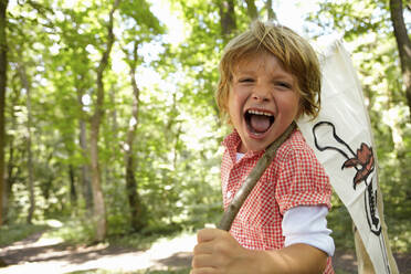 Portrait of screaming boy carrying pirate flag in forest - AUF00206