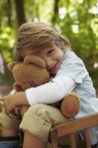 Porträt eines Jungen, der einen Teddybär im Wald umarmt, lizenzfreies Stockfoto