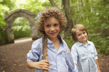 Portrait of boy with wood stick and friend in forest - AUF00226