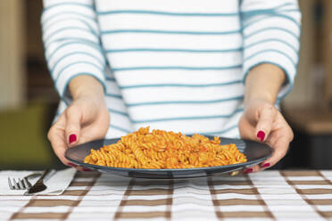 Woman serving pasta on plate at home - WPEF02745