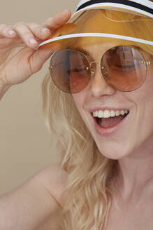 Portrait of happy young woman wearing sunglasses and sun visor - PGCF00074