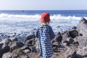 Back view of little girl standing at water's edge looking at the sea, La Gomera, Canary Islands, Spain - IHF00304