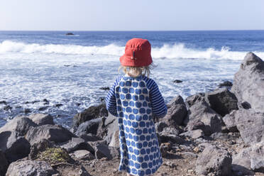 Rückenansicht eines kleinen Mädchens, das am Ufer steht und auf das Meer schaut, La Gomera, Kanarische Inseln, Spanien - IHF00304