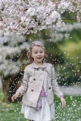 Porträt eines glücklichen kleinen Mädchens in einem Park, das unter einem blühenden japanischen Kirschbaum steht - OGF00265