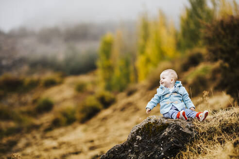 Glücklicher kleiner Junge auf einem Felsen in herbstlicher Natur sitzend - LJF01490