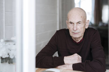 Portrait of pensive old man sitting at table looking out of window - EYAF01000