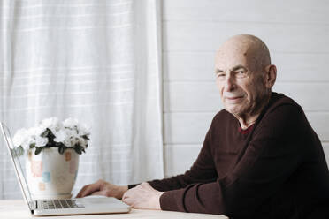 Porträt eines lächelnden alten Mannes, der mit einem Laptop am Tisch sitzt - EYAF01003