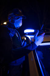 Polizist bei einem Notfalleinsatz, mit Gesichtsmaske und Telefon in der Hand - OCMF01167