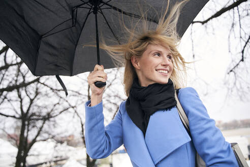 Smiling blond woman holding umbrella in storm - PNEF02503